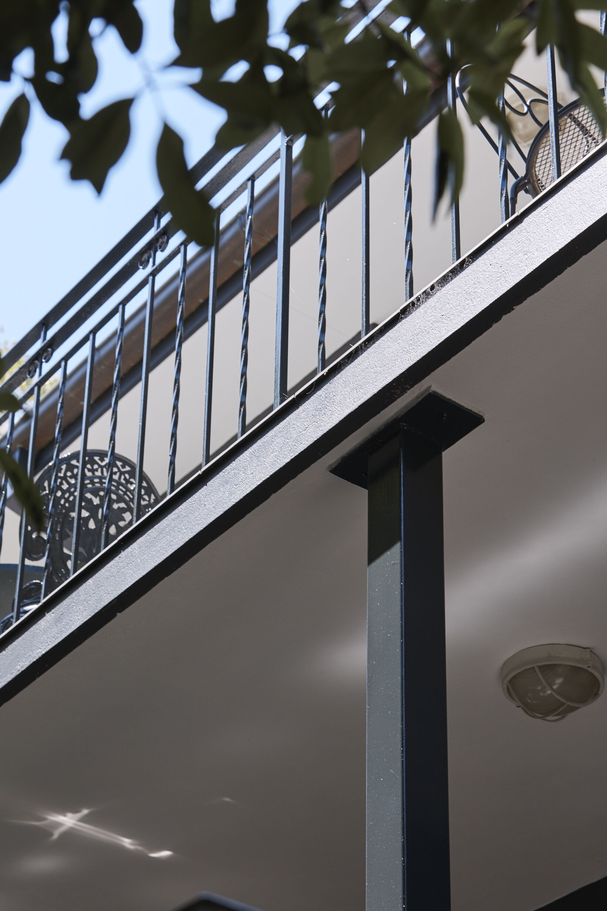 A metal balcony railing with a circular window, a white wall, and a ceiling vent.