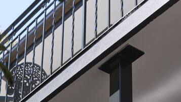 A metal balcony railing with a circular window, a white wall, and a ceiling vent.