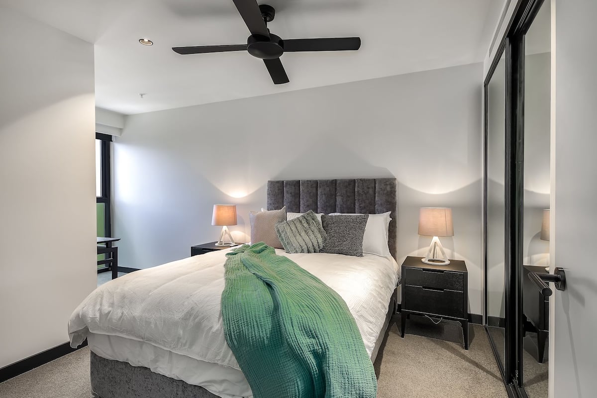 A modern bedroom with a bed, two bedside tables, a ceiling fan, and a large mirror.