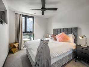 Une chambre à coucher moderne avec un lit, une table de chevet, une lampe, un ventilateur de plafond et une fenêtre avec des rideaux.