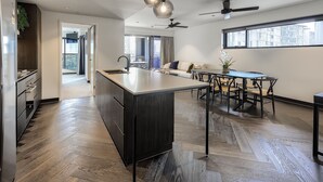 Une cuisine moderne dotée d’un îlot central, d’un coin repas avec une table et des chaises, et d’une grande fenêtre offrant une vue sur la ville.