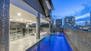 Une piscine à débordement située sur le toit, offrant une vue sur les gratte-ciel de la ville, une architecture moderne et un espace salon couvert.