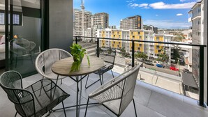 Un balcon avec une table ronde et des chaises, un pot de fleurs et une vue sur les bâtiments environnants.