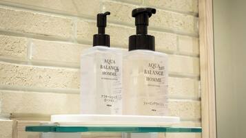 Two bottles of Aqua Balance Homme on a glass shelf against a white brick wall.