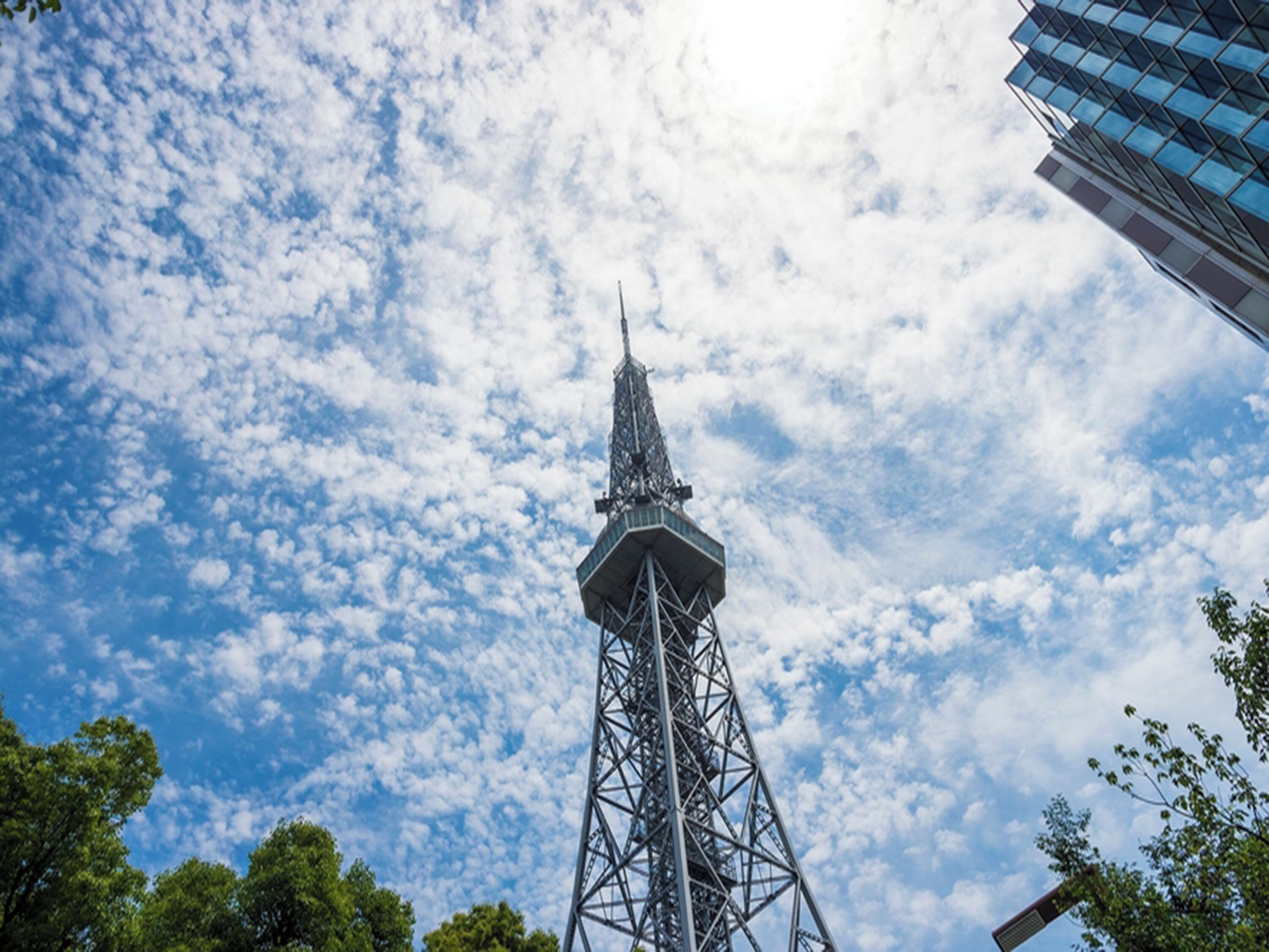 A tall, metal tower with a pointed top, set against a backdrop of a blue sky with scattered clouds.