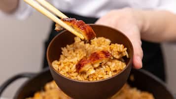 A bowl of rice with a piece of meat being held by chopsticks.