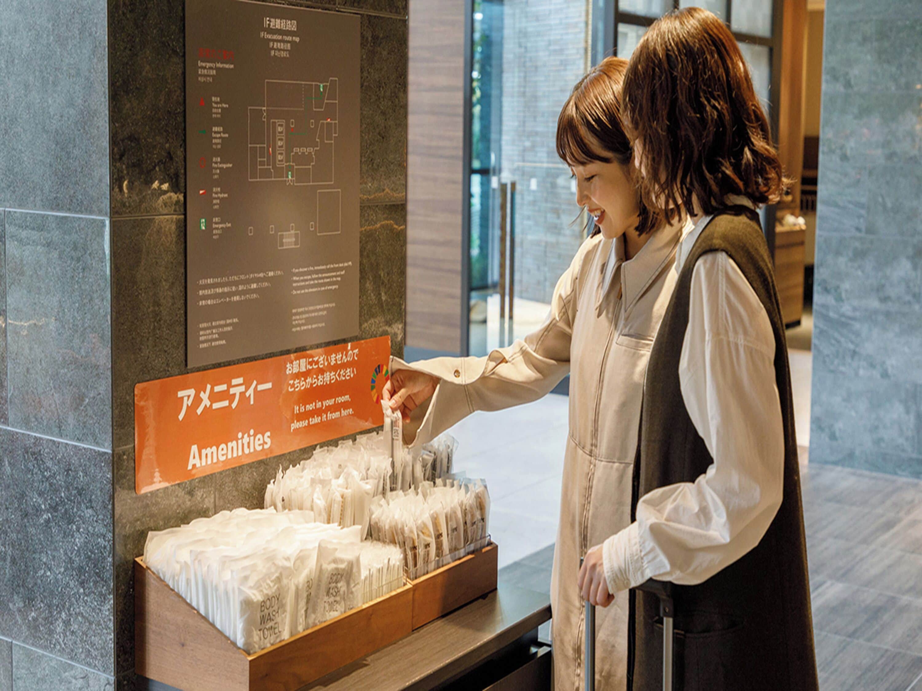 A person at a hotel reception desk with a sign indicating amenities and a display of toiletries.
