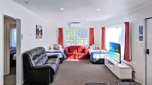 A hotel room with a bed, a sofa, a red armchair, a TV, and a dining table. - ASURE Kaimai View Motel (Katikati)
