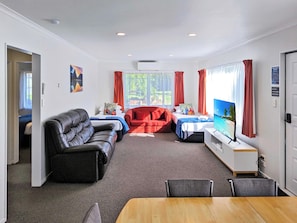 Una habitación de hotel con una cama, un sofá, un sillón rojo, un televisor y una mesa de comedor.