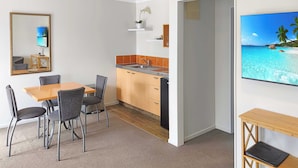 A modern kitchen with a wooden countertop and cabinets, a dining area with a table and chairs, and a large flat-screen TV mounted on the wall. - ASURE Kaimai View Motel (Katikati)