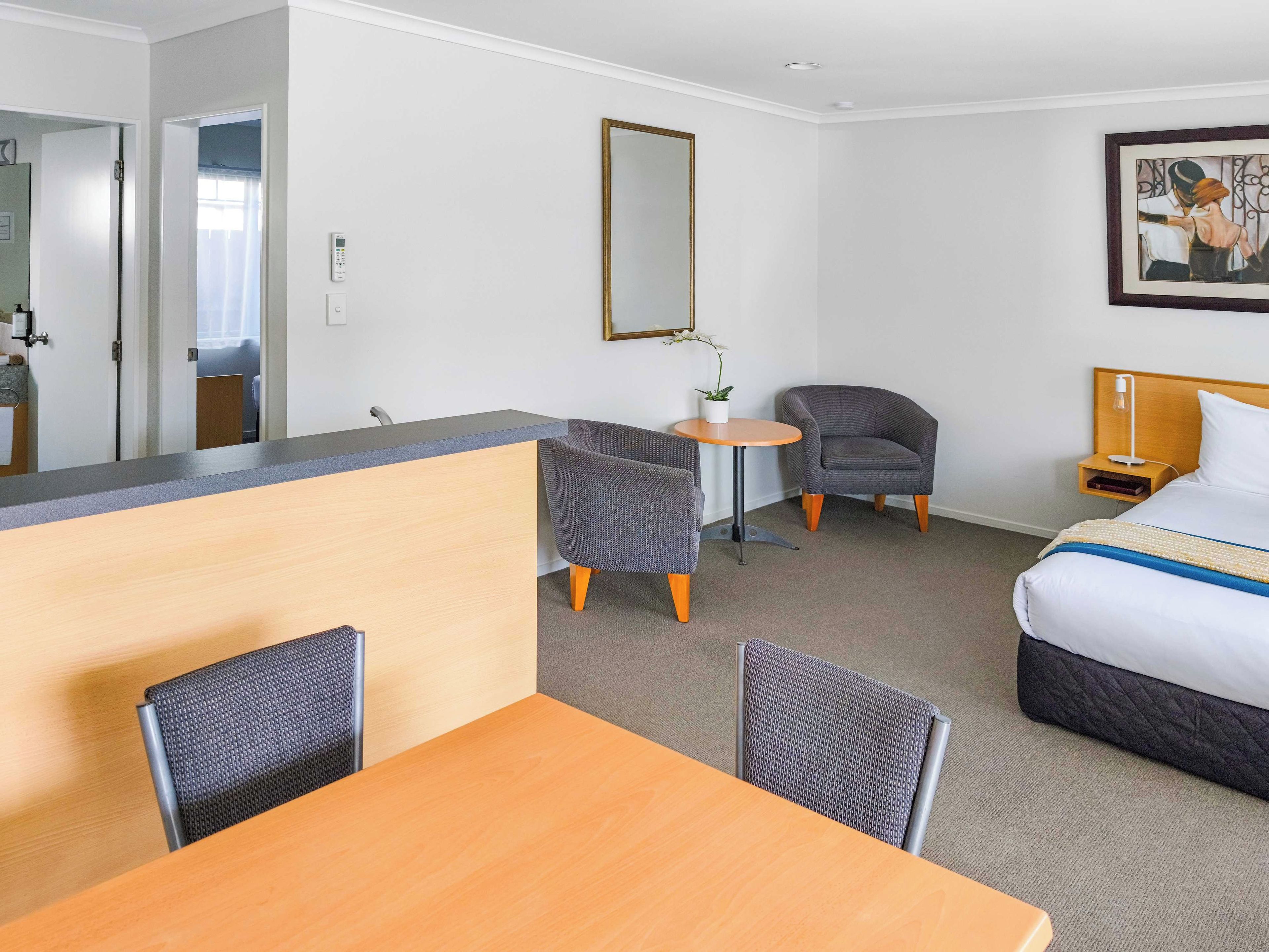 Ein Hotelzimmer mit einem Bett, einem Schreibtisch, zwei Stühlen, einem kleinen Tisch mit einer Pflanze und einem Nachttisch mit einer Lampe.