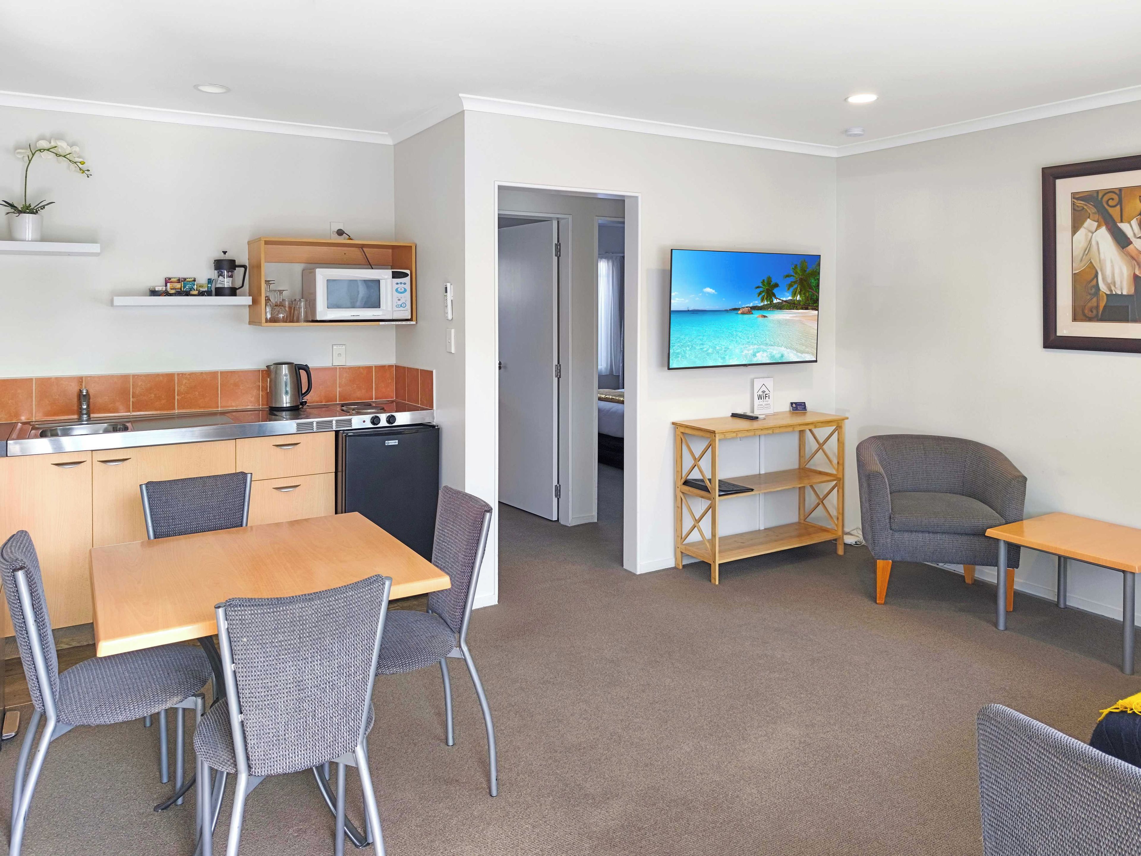 Un espacio habitable compacto con kitchenette, comedor y televisor montado en la pared.