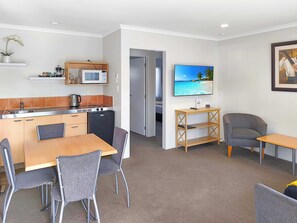 A compact living space with a kitchenette, dining area, and a TV mounted on the wall. - Kaimai View Motel (Katikati)