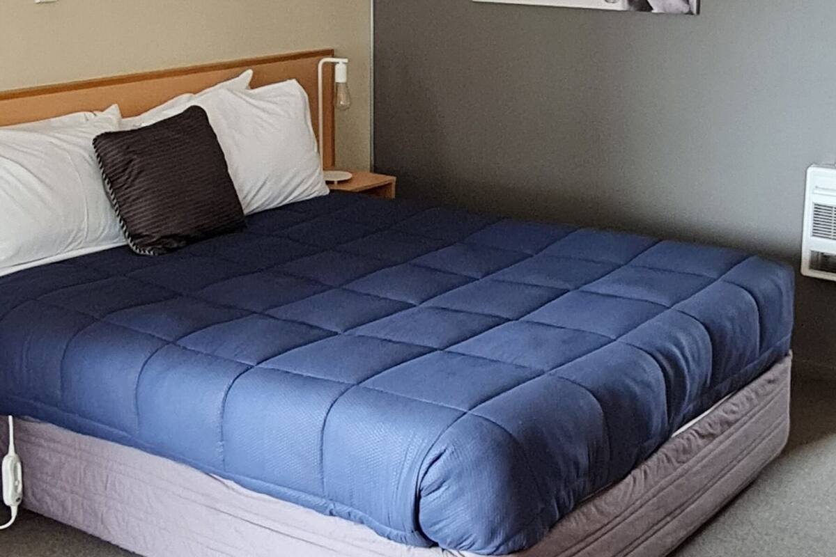 A bedroom with a large bed, a nightstand, a wall-mounted light, and a horse painting.