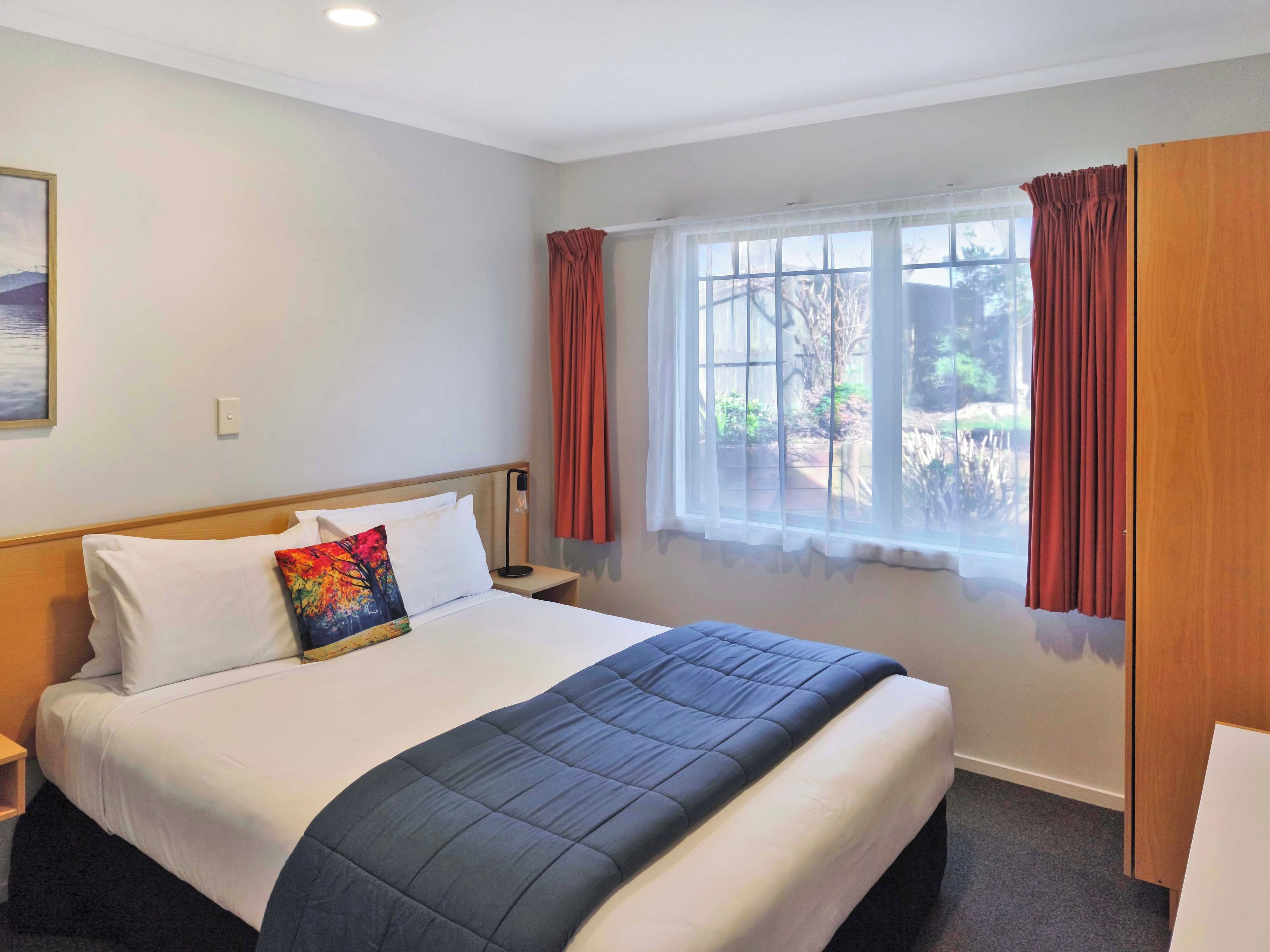 A hotel room with a large bed, a window with curtains, a bedside table, and a nightstand.