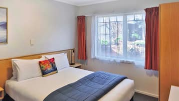 A hotel room with a large bed, a window with curtains, a bedside table, and a nightstand.