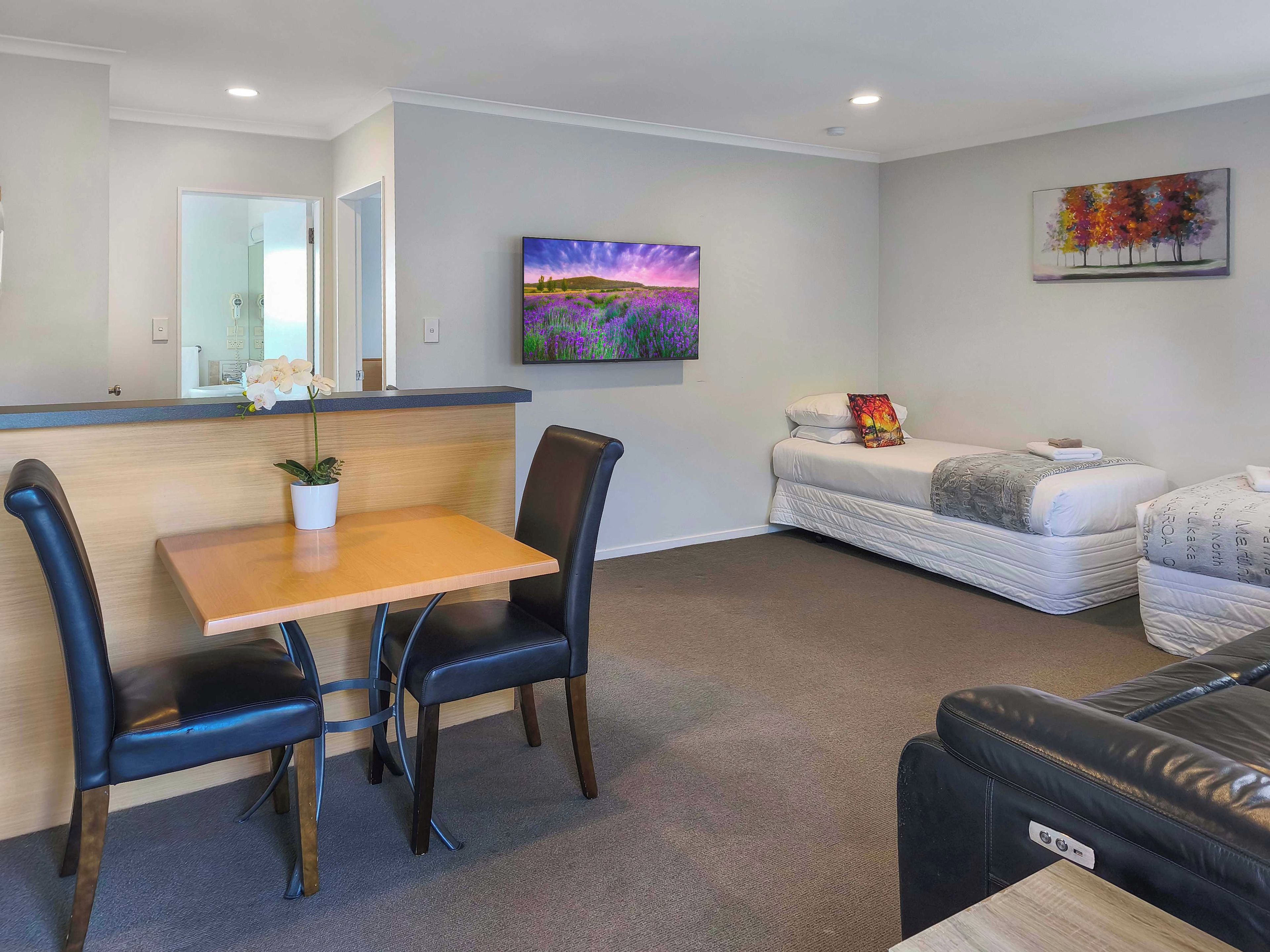 A modern living room with a sofa, a dining table with chairs, a flat-screen TV, and a painting on the wall.