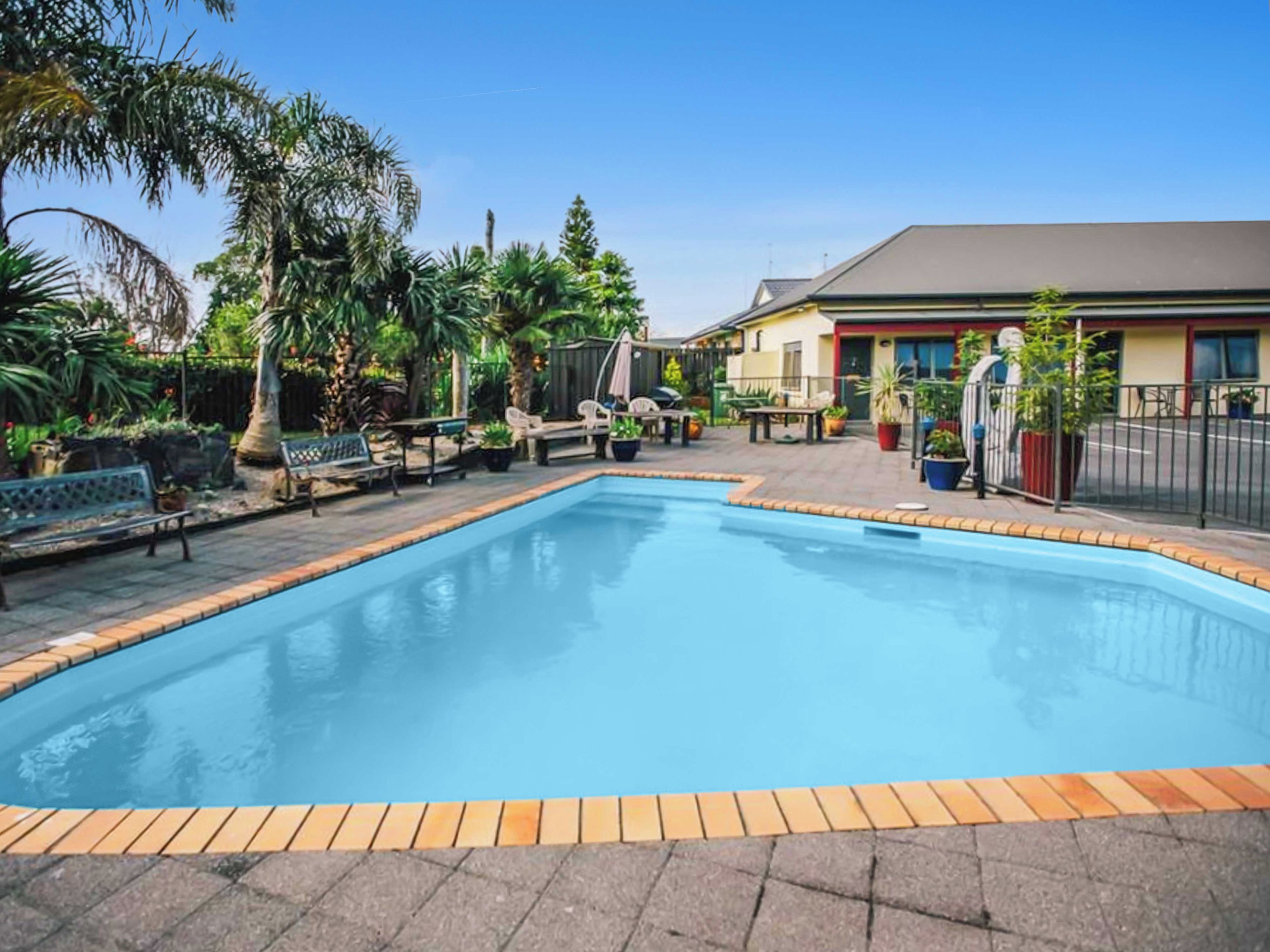 A swimming pool with a tiled edge, surrounded by outdoor furniture and potted plants.
