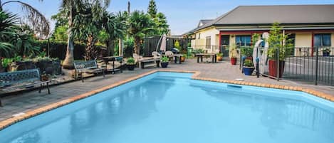 Una piscina con borde de azulejos, rodeada de mobiliario de exterior y plantas en macetas.
