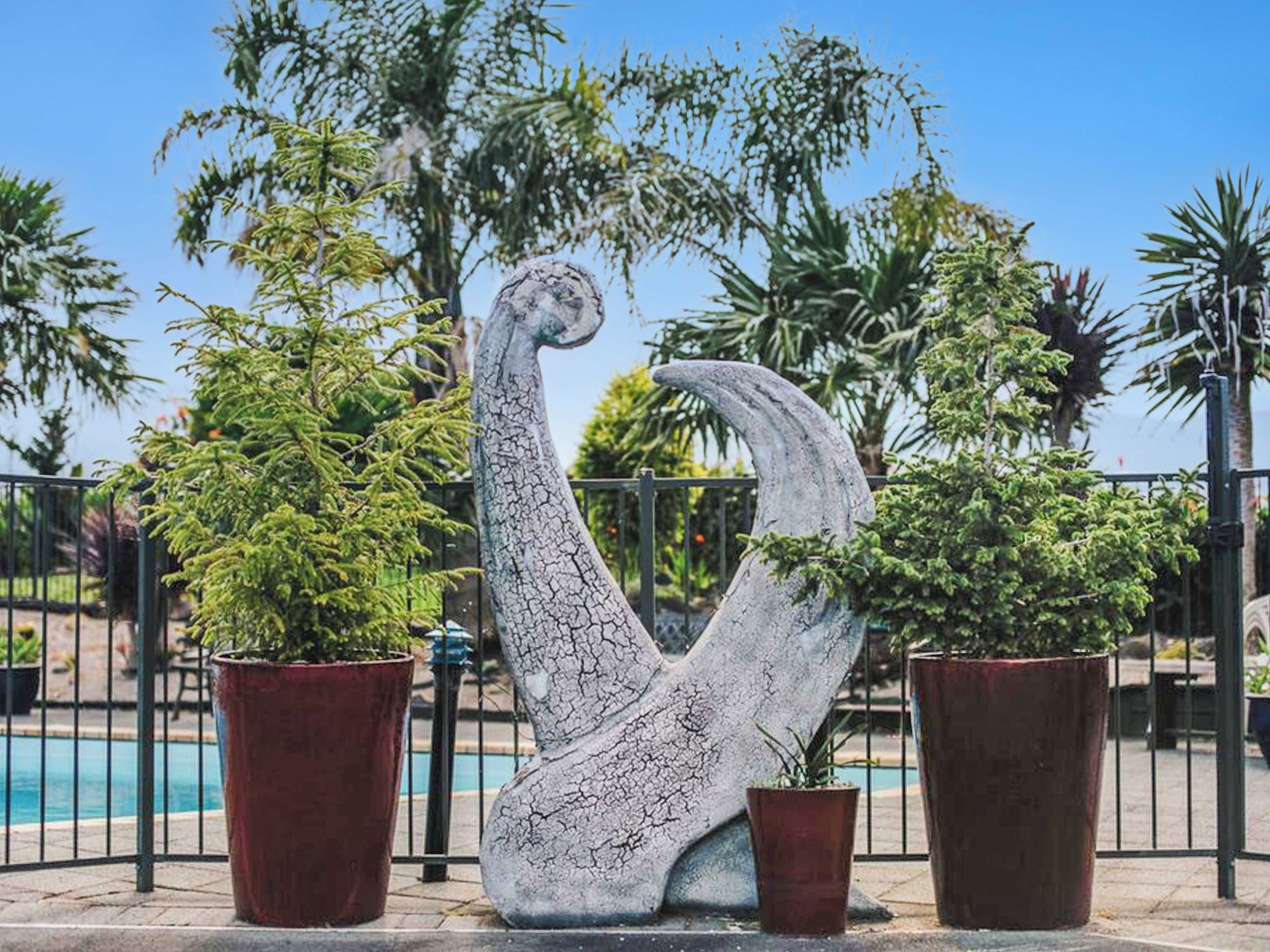 A sculpture of a bird in a curved position with two potted plants beside it.