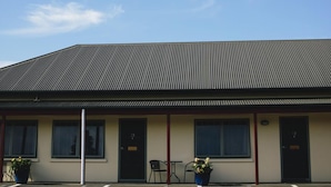 Ein Gebäude mit Wellblechdach, mehreren Fenstern und einer Tür mit einer Hausnummer. Vor der Fassade stehen Pflanzkübel.