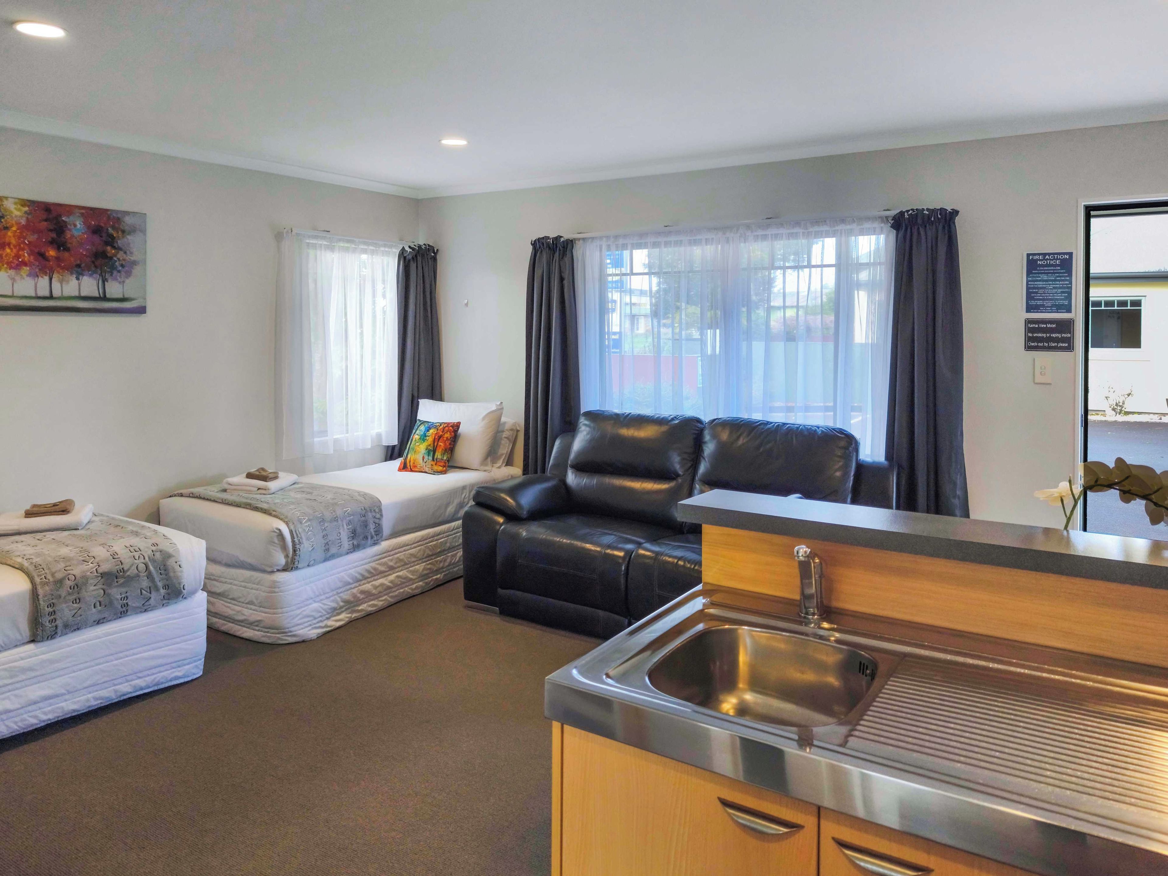 Habitación compacta con cama, sofá, kitchenette pequeño y ventana con cortinas.