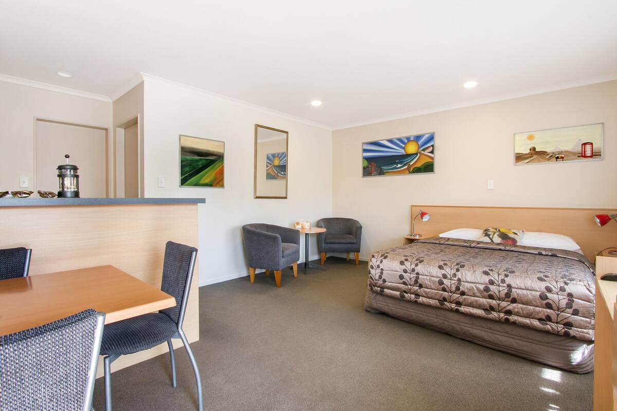A hotel room with a bed, a desk, two chairs, a small table, and artwork on the walls.