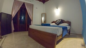 A bedroom with a wooden bed, a nightstand, a wardrobe, a mirror, and a window with curtains. - Girilena Guest House (Hikkaduwa)