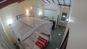 A room with a bed under a mosquito net, a bedside table, a mirror, and a small plant. - Girilena Guest House (Hikkaduwa)