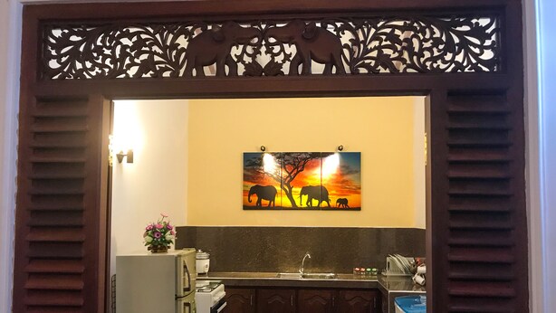A kitchen with a refrigerator, stove, sink, and cabinets. There is a decorative panel above the sink with elephant designs. - Girilena Guest House (Hikkaduwa)