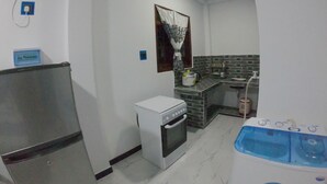 A compact kitchen with a refrigerator, oven, and washing machine. - Girilena Guest House (Hikkaduwa)