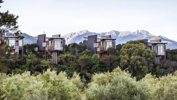 Un edificio moderno de varios pisos con múltiples balcones, rodeado de exuberante vegetación y montañas al fondo.