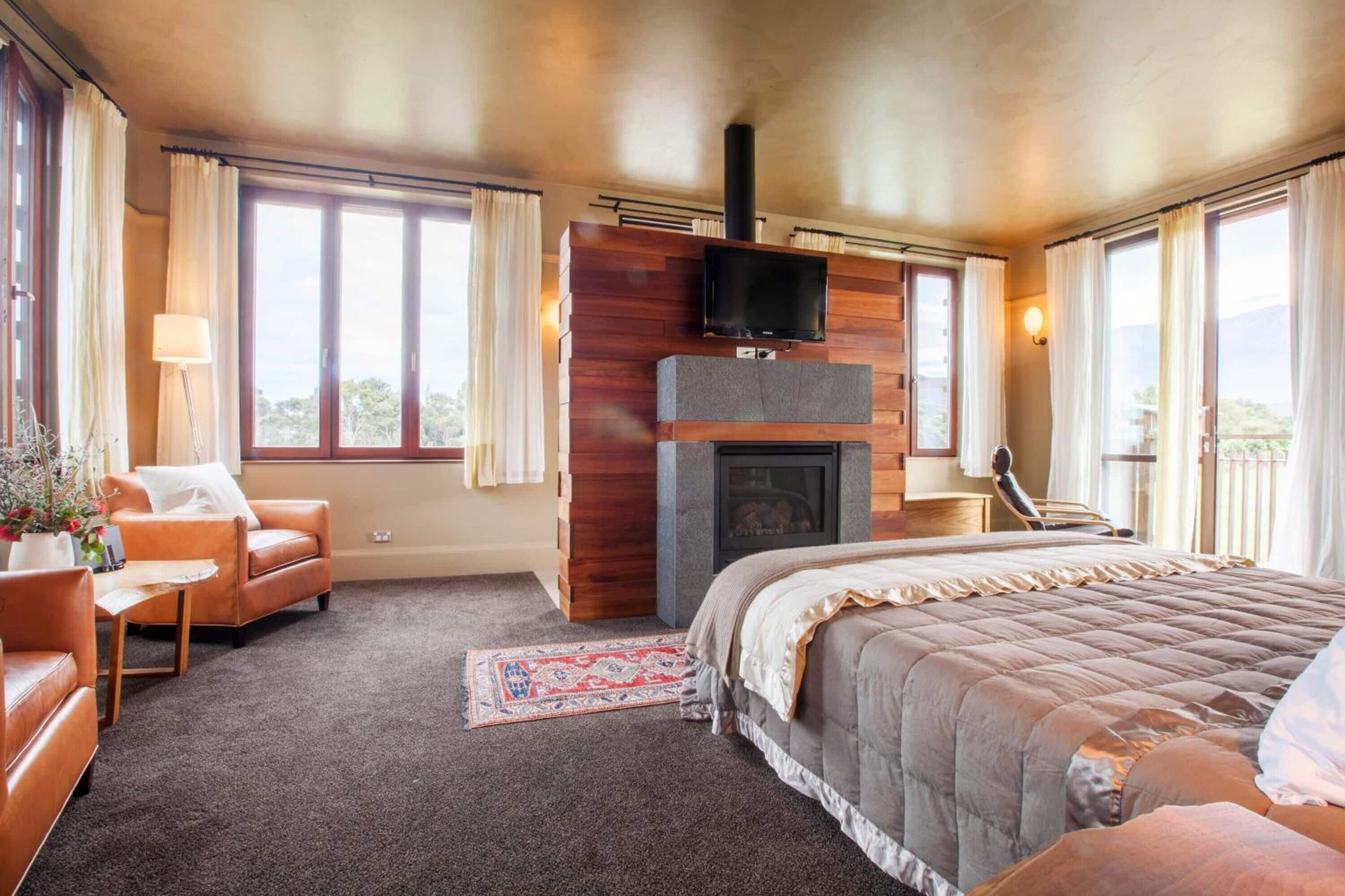 A spacious bedroom with a large bed, a fireplace, a television, and a balcony with curtains.