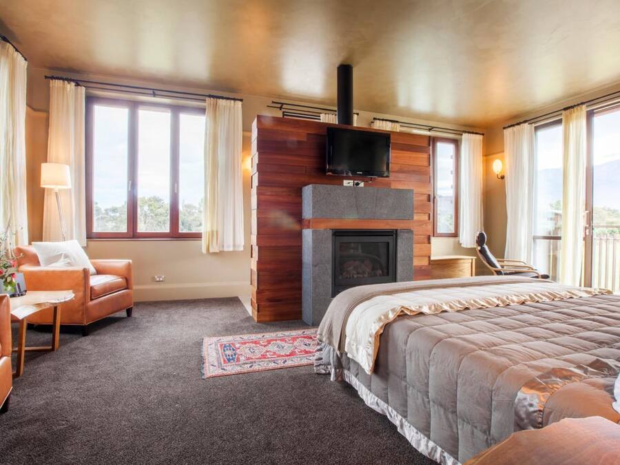 A spacious bedroom with a large bed, a fireplace, a television, and a balcony with curtains.