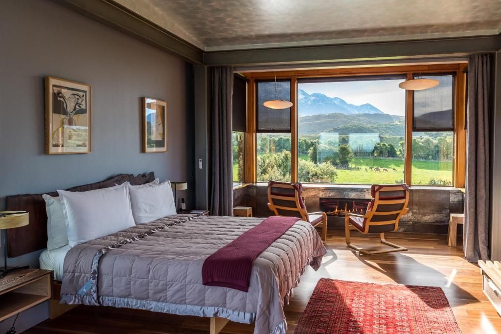 A bedroom with a large bed, a view of the outdoors, and a seating area by the window.