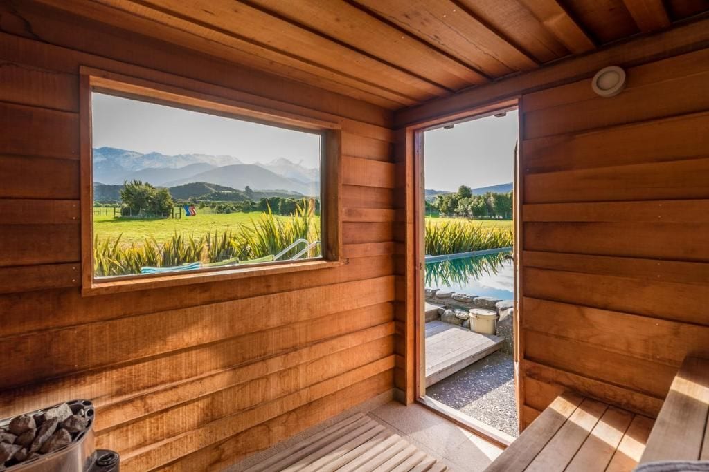 Una cabaña de madera con un ventanal grande que ofrece vistas a un campo y montañas.