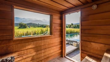 Una cabaña de madera con un ventanal grande que ofrece vistas a un campo y montañas.
