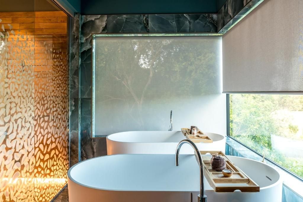 A modern bathroom with a large freestanding bathtub, a smaller sink, and a window providing a view of greenery.