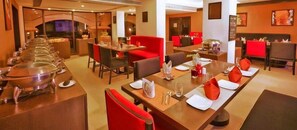 A restaurant with multiple dining tables, red cushioned chairs, and buffet service. - Gateway Varkala - Ihcl Seleqtions (Varkala)