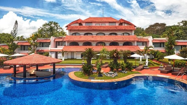 A hotel with a large swimming pool, multiple balconies, and lush landscaping.