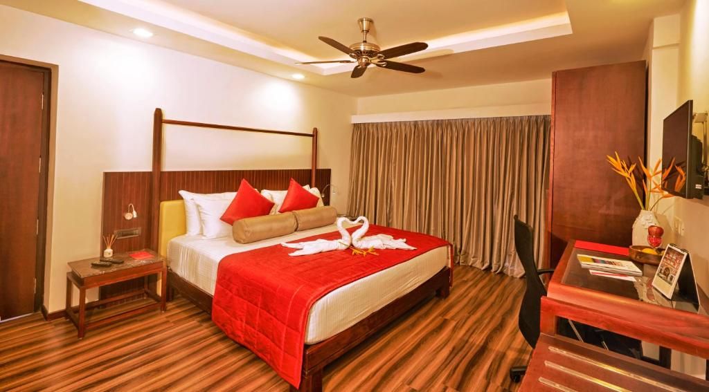 A hotel room with a bed, a desk, a chair, a ceiling fan, and a curtain.