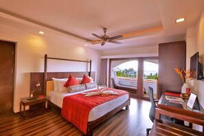 A hotel room with a bed, a desk, a chair, a ceiling fan, and a view of the outdoors. - Gateway Varkala - Ihcl Seleqtions (Varkala)