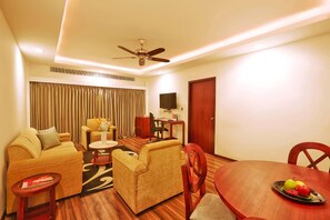 A hotel room with a sofa set, a dining table with fruit, a TV, and a ceiling fan. - Gateway Varkala - Ihcl Seleqtions (Varkala)
