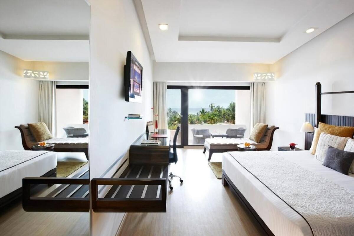 A hotel room with two beds, a desk, a chair, and a balcony with a view.