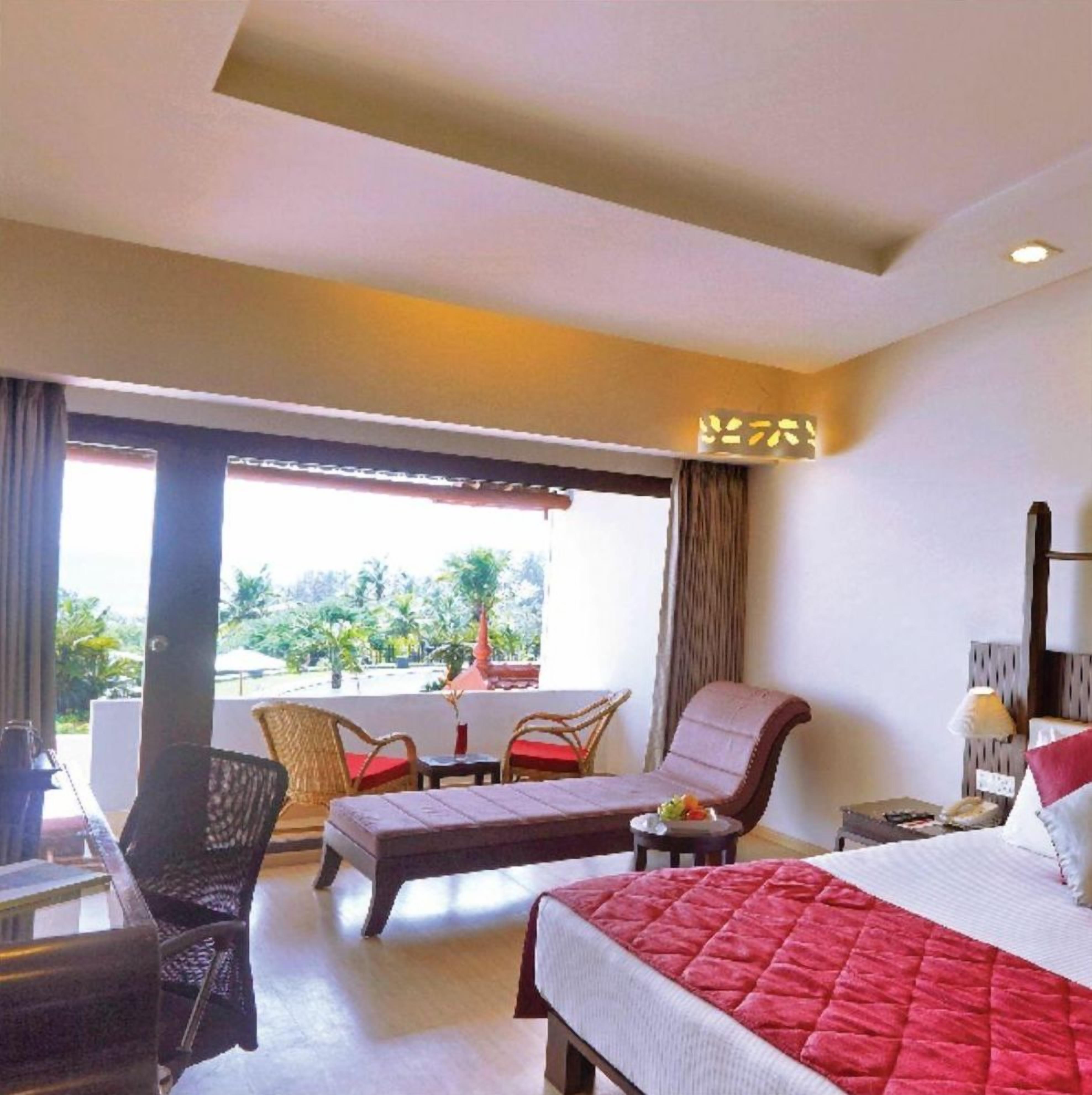 A hotel room with a bed, a sofa, a chair, a small table, and a window with a view of greenery.