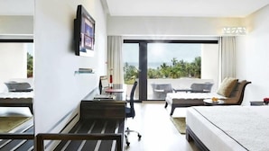 A modern hotel room with a bed, a desk, a chair, a sofa, and a large window offering a view of the outdoors.