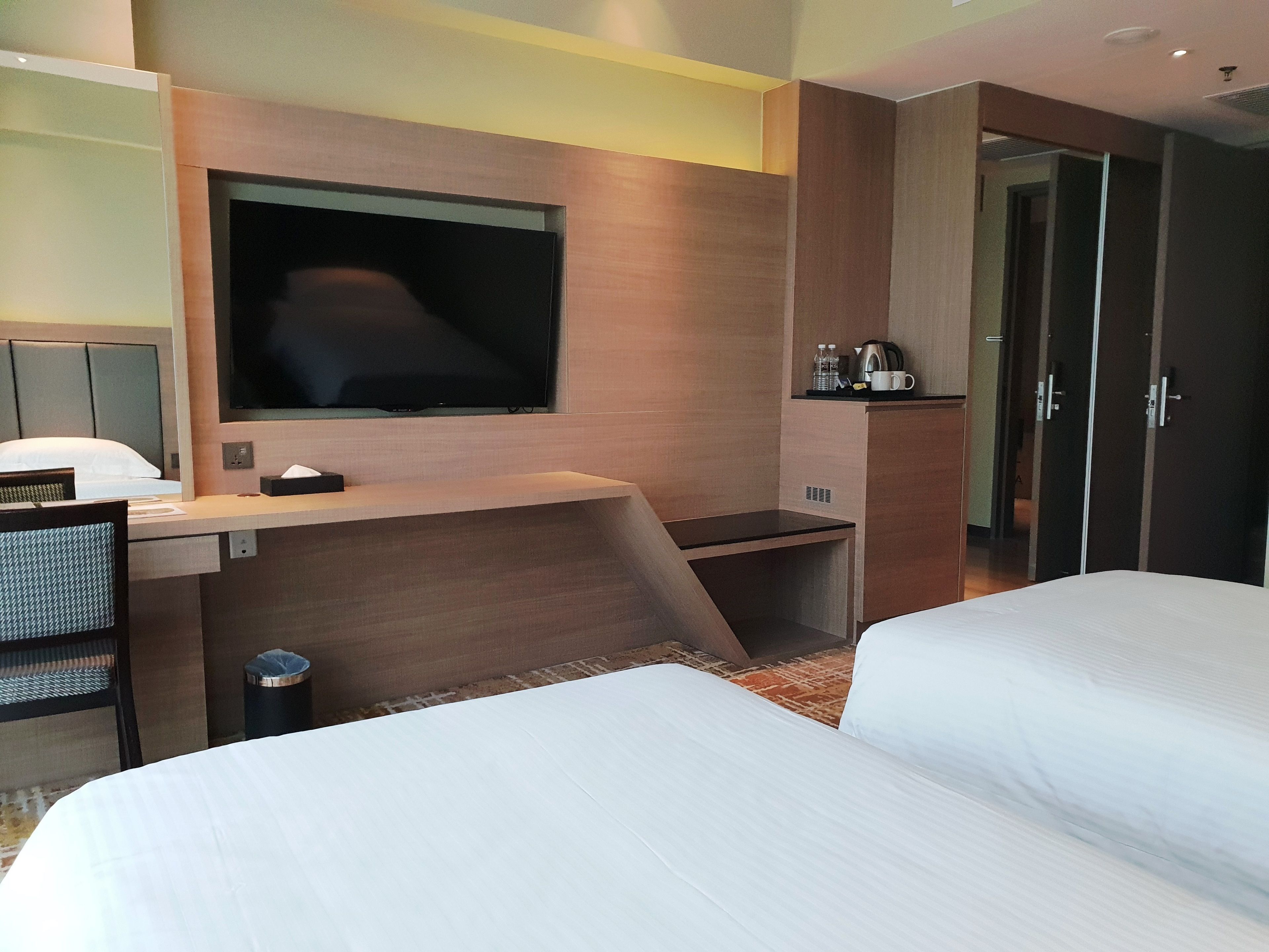 A hotel room with a bed, a desk with a flat-screen TV, a coffee maker, and a wardrobe.