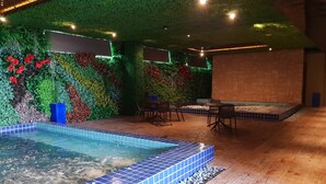 An indoor pool area with tiled flooring, a seating area with chairs, and a wall decorated with various plants and flowers. - KSL Hot Spring Resort (Johor Bahru)