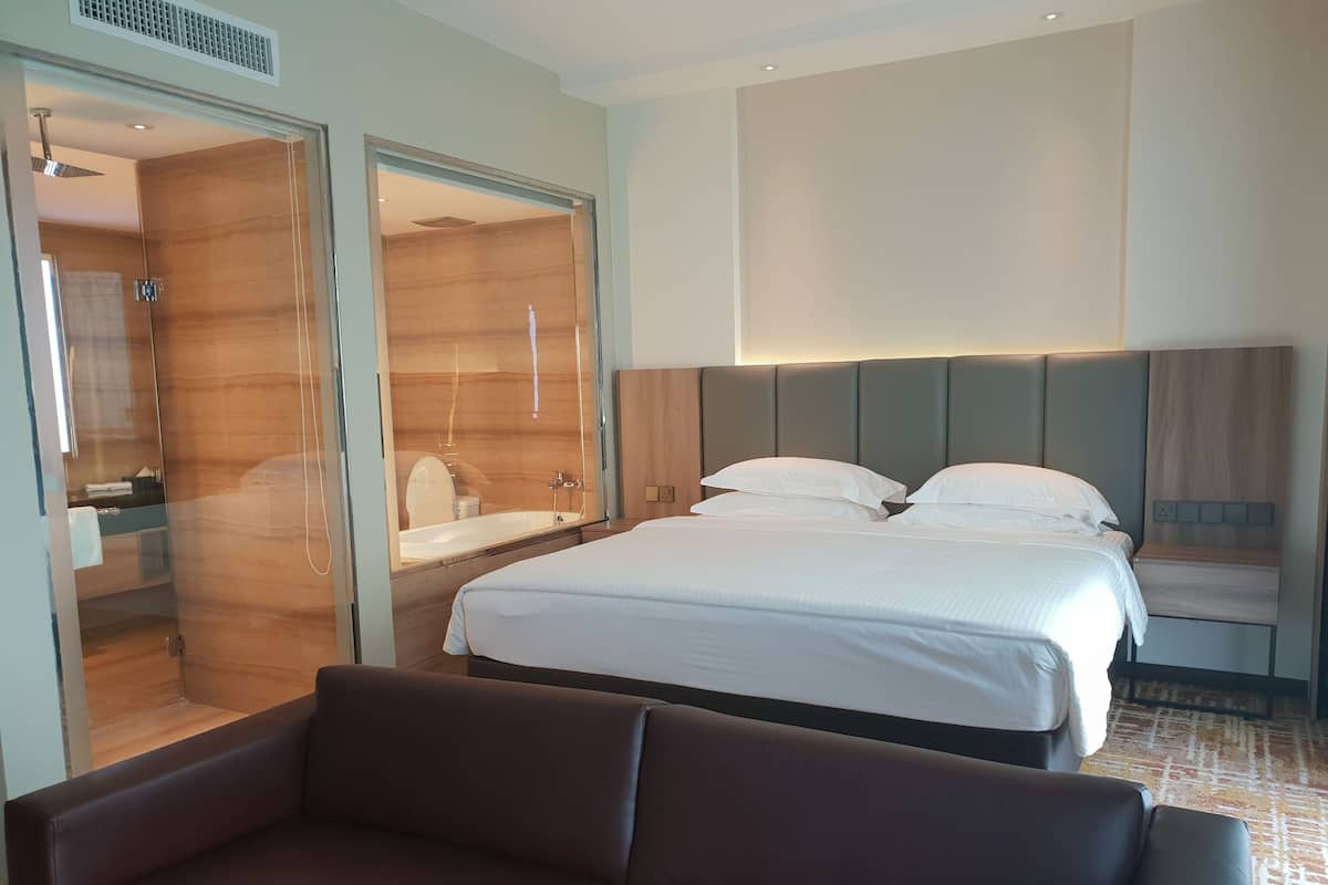 A modern hotel room with a large bed, a sofa, a walk-in shower, and a large mirror.