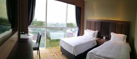 A hotel room with two beds, a desk, and a large window offering a view of the city.